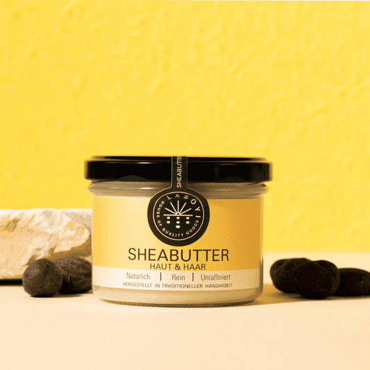 Unraffinierte Sheabutter im Glas vor gelbem Hintergrund