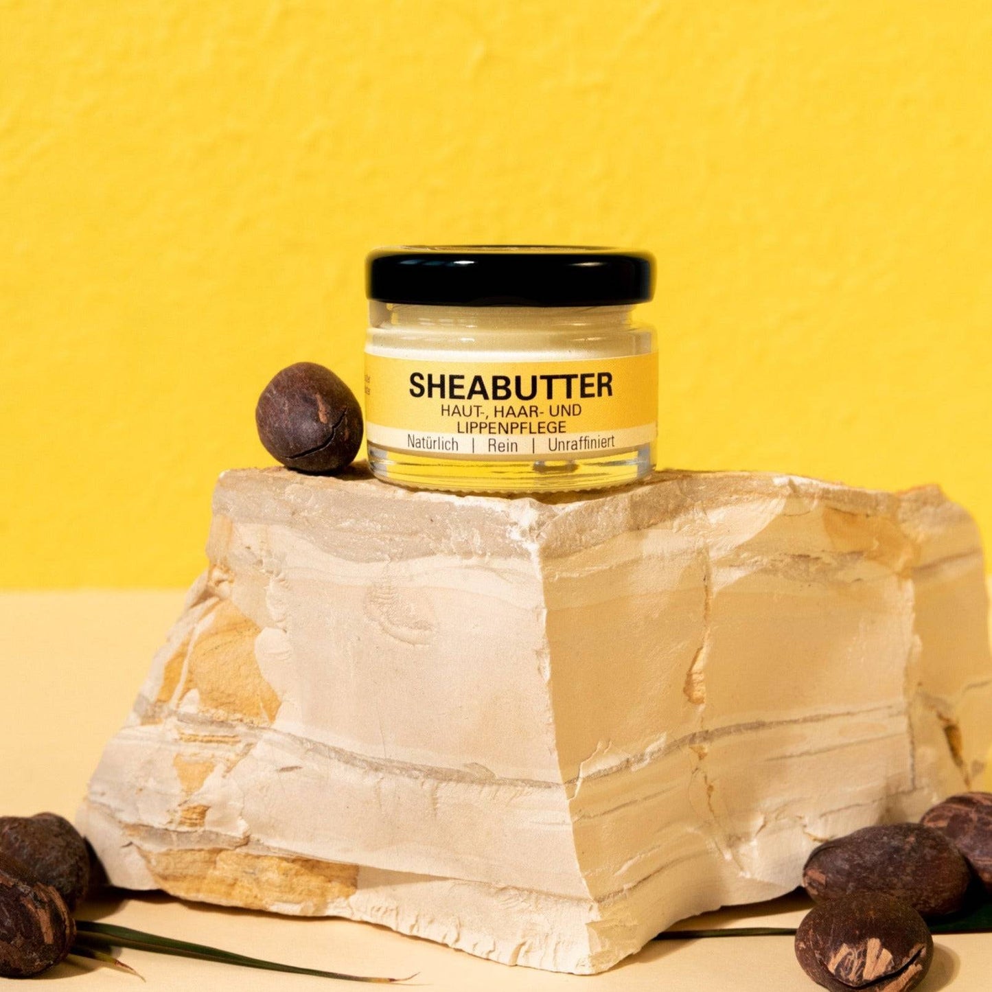 Sheabutter im Glastiegel auf Stein vor gelbem Hintergrund