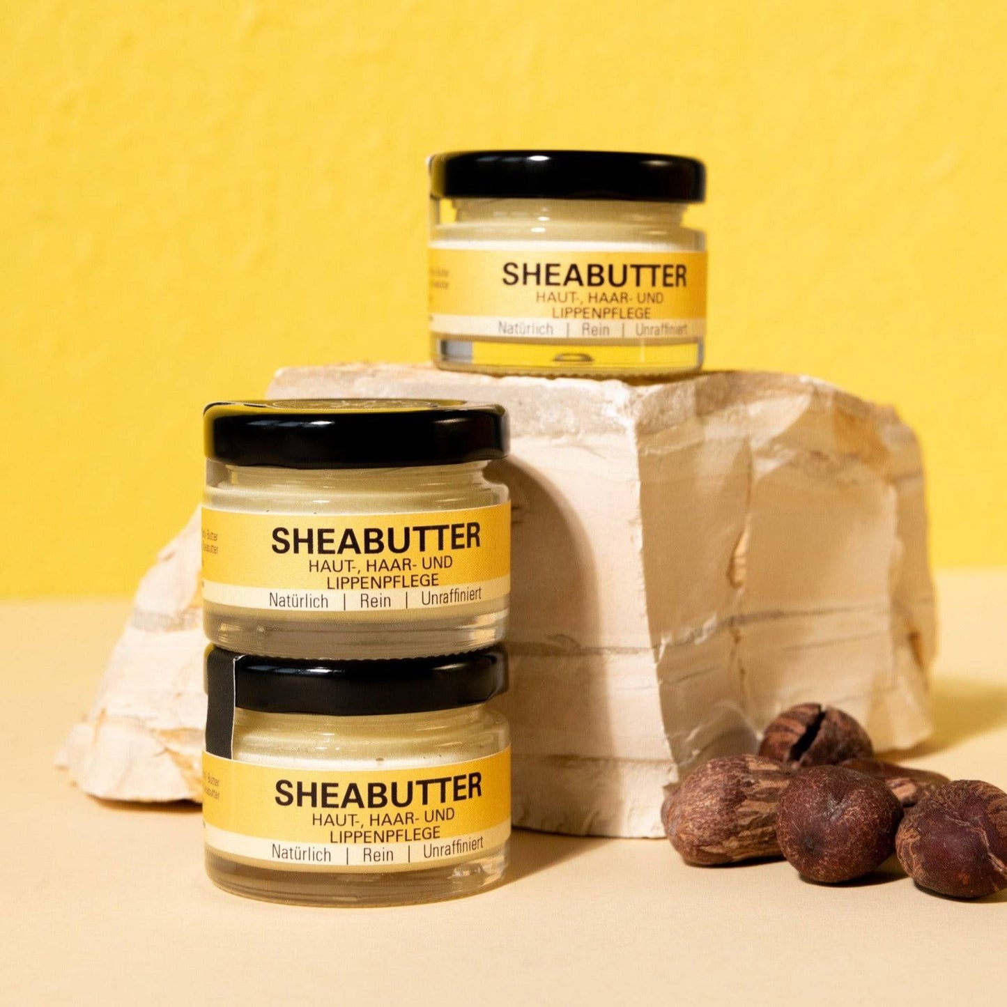 Drei Sheabutter-Tiegel auf Stein mit Nüssen